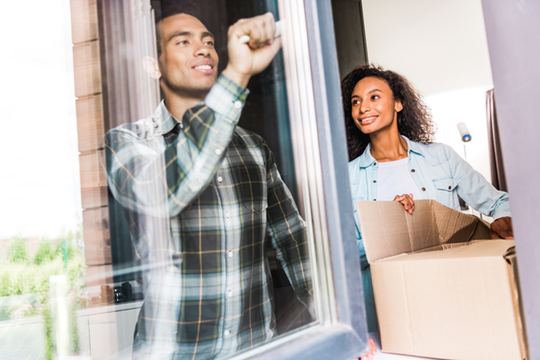 african american husband opening window while wife opening box and looking at husband - Photo, Image