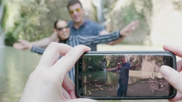 Pareja tomando fotos con un teléfono cerca de una cascada
 - Imágenes, Vídeo