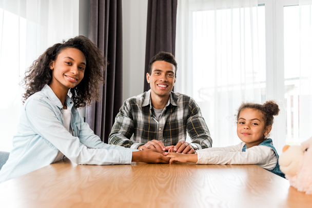 Африканская американская семья сидит перед столом, улыбается и смотрит в камеру
 - Фото, изображение