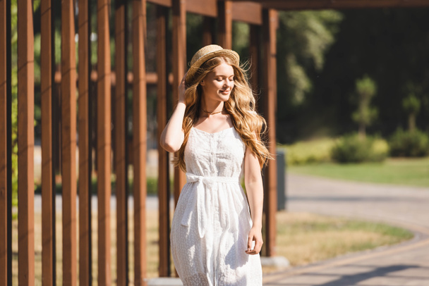 beautiful girl in white dress touching straw hat and smiling with closed eyes  - Fotoğraf, Görsel
