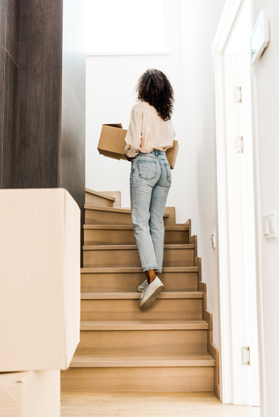 back view of woman walking upstairs while holding box  - Fotoğraf, Görsel