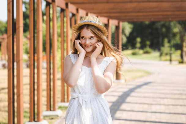 hermosa chica en vestido blanco y sombrero de paja sonriendo y mirando hacia otro lado
 - Foto, Imagen