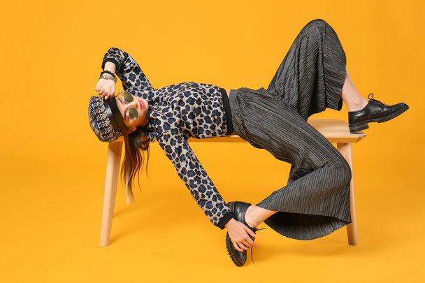 Giovane donna alla moda sdraiata su panchina contro lo sfondo di colore
 - Foto, immagini