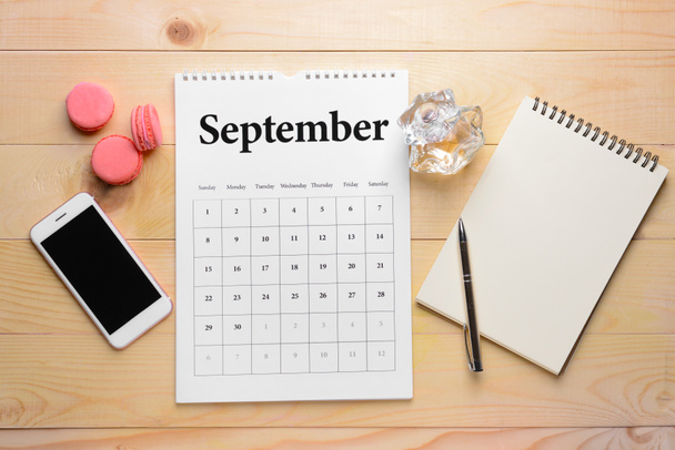 Flip papieren kalender, mobiele telefoon, notebook en cakes op houten achtergrond - Foto, afbeelding