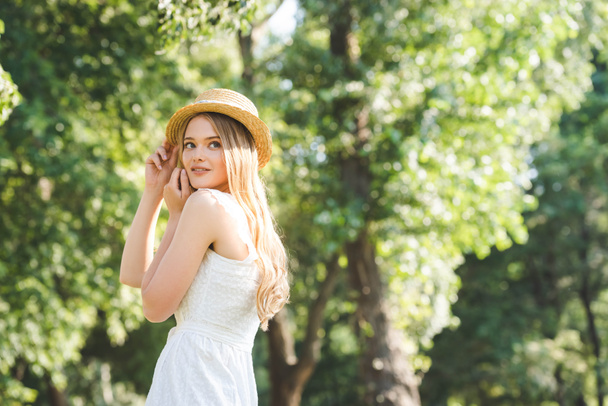 beautiful young girl in white dress and straw hat smiling and looking away - Photo, image