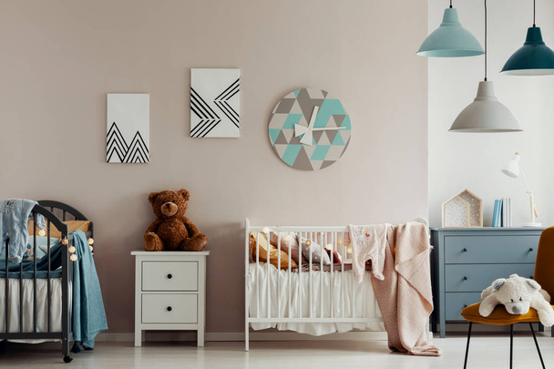 A teddy bear, two beds and a large clock on a beige wall in bright and warm bedroom interior for twins. Real photo - 写真・画像
