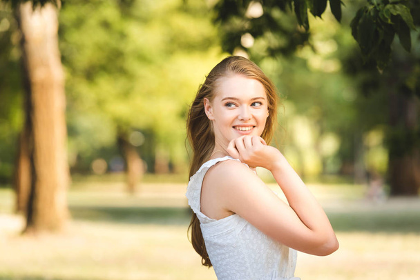 beautiful young girl in white dress posing while standing in park and looking away - Photo, Image