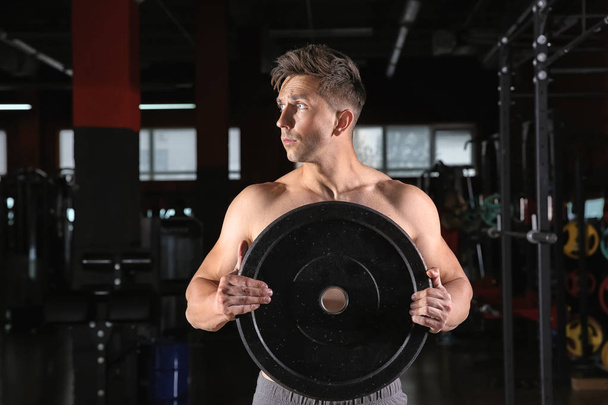 Sporty young man training with weight plate in gym - Photo, image