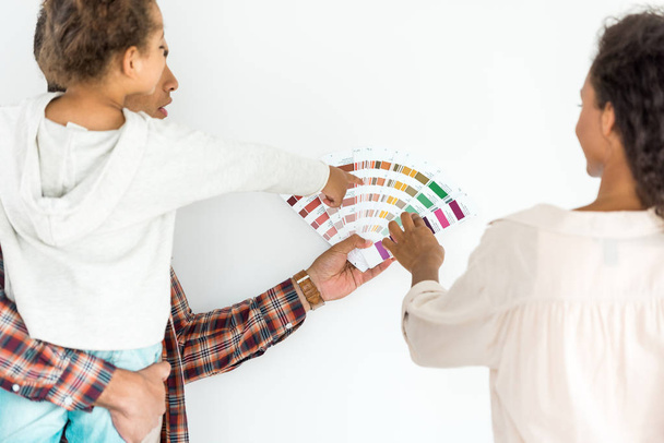 african american family trying to choose color for their wall from colorful palette isolated on white - Foto, Imagem