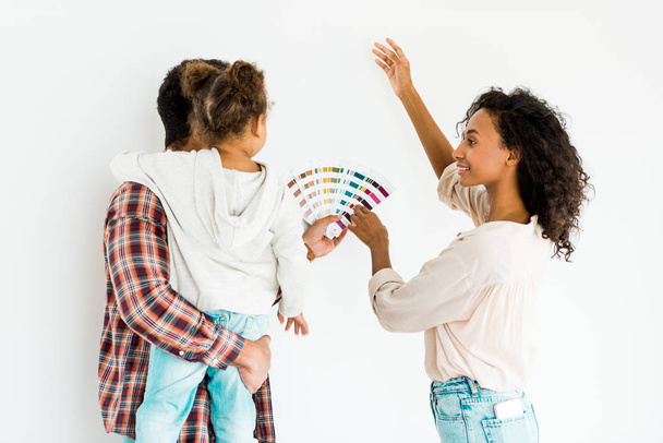 afroamericano mostrando qualcosa con la mano e tenendo tavolozza colorata mentre papà tenendo bambino isolato su bianco
 - Foto, immagini