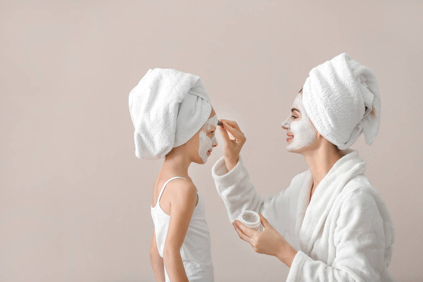 Mother applying cream onto face of her little daughter against grey background - 写真・画像