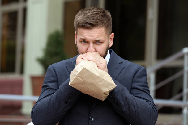 Businessman with paper bag having panic attack outdoors - Photo, Image