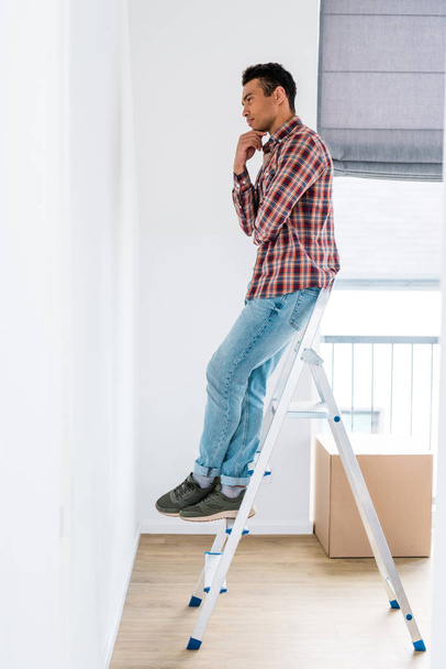 full length view of handsome african american man standing at ladder and looking at wall - Photo, Image