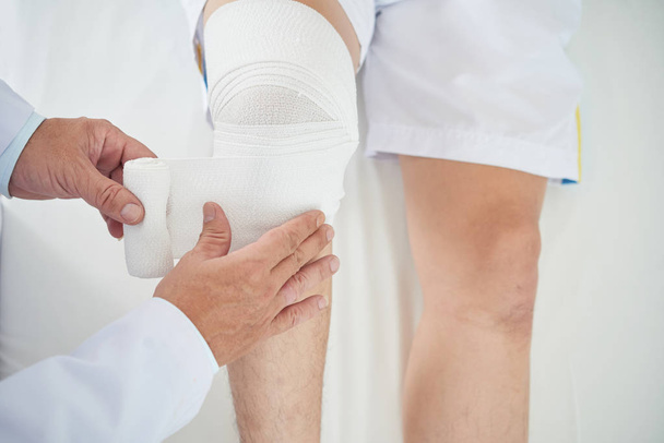 Imagem recortada do médico aplicando bandagem na perna do paciente
 - Foto, Imagem