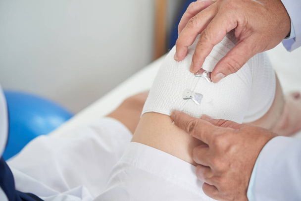 Imagen de primer plano del médico que aplica vendaje elástico en la rodilla
 - Foto, Imagen