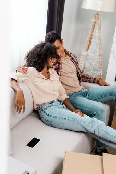 high angle view of african american wife and husband relaxing while hugging and sitting on sofa  - Foto, afbeelding
