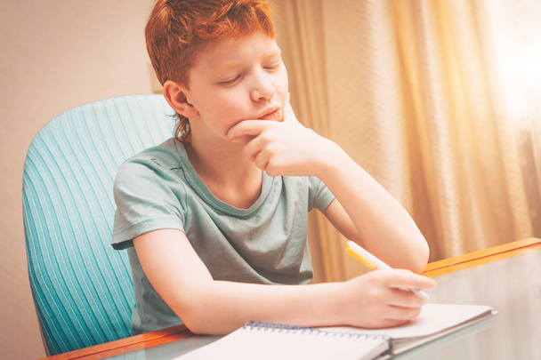 Red-haired boy reflected in the process of working on a school homework - Foto, Bild