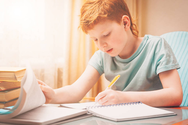 Home schooling, red-haired boy learns writing down in a workbook - Fotó, kép