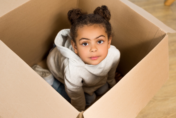 high angle view of cute child sitting in box and looking at camera  - Photo, Image