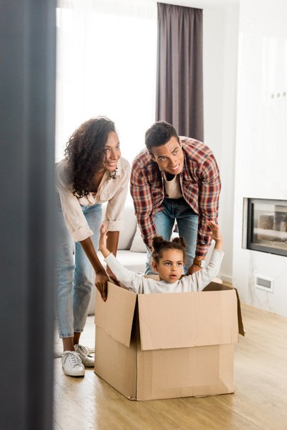 full length view of african american parent moving box with daughter  - Photo, Image