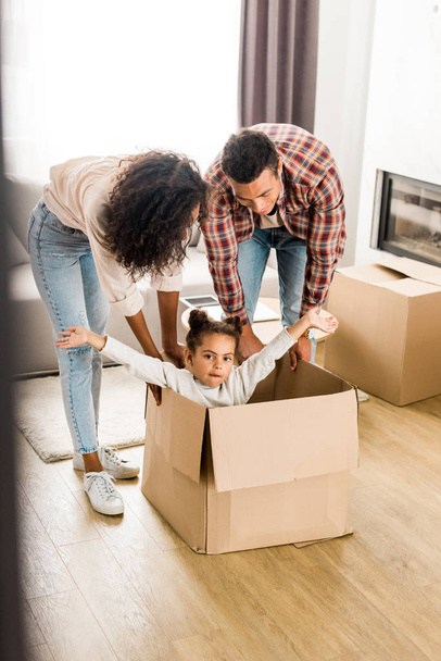  foco seletivo de pais afro-americanos brincando com a filha, movendo caixa com criança
  - Foto, Imagem