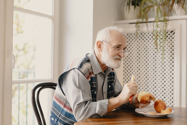 Lonely elderly man eating an apple by the table in empty home - Photo, image