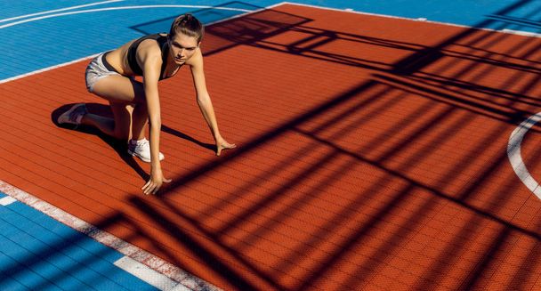 Blond sporty female runner to quick start position on a stadium. - Valokuva, kuva
