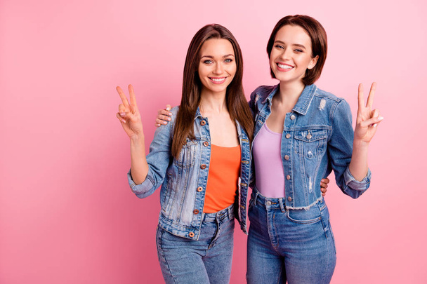 Close up photo two beautiful funky sisters she her best ladies pretty appearance party chill mood hugging v-sign symbol say hi hello wear jeans denim jackets blazers isolated bright pink background - Foto, Imagem