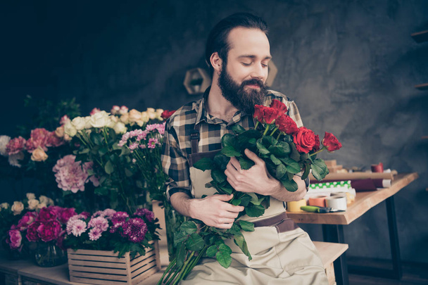 Portrait of his he nice attractive content cheerful cheery dreamy guy gardener enjoying life lifestyle holding in hands beautiful trendy red bouquet at modern industrial loft concrete style - Foto, immagini