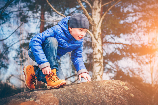 A young ranger in hiking boots climbs the rocks in search of adventure, discoverer and explorer - Zdjęcie, obraz
