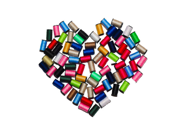 Spools with multicolored threads in the shape of a heart on a white background. Isolate view from above - Photo, Image