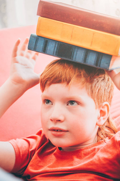 The red-haired child holds several books on his head, the severity of knowledge - Zdjęcie, obraz