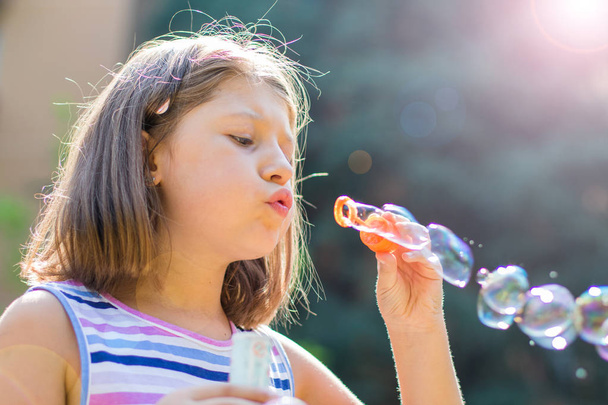 Girl blowing soap bubbles in park in a sunny day - Valokuva, kuva