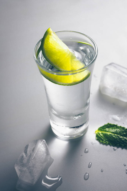 A glass of vodka with a lime slice and a mint leaf, delicious alcohol - Фото, зображення