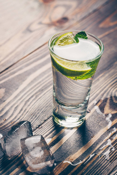 Cold gin in a glass on a wooden table with a slice of lime, mint and ice slices - Foto, Imagem