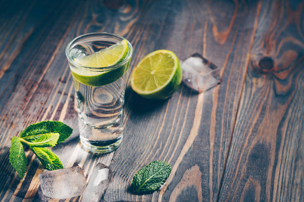 A glass of vodka with lime on a rustic wooden table - Foto, imagen