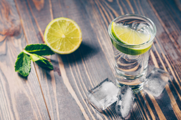 A cold glass of vodka on a table with lime and lemon - Zdjęcie, obraz