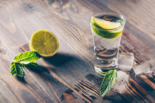 A cold glass of tequila on a table with lime and lemon - 写真・画像