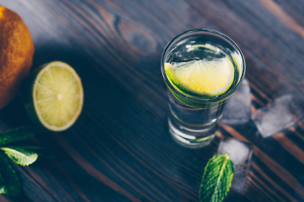 Cold tequila in a glass on a wooden table with a slice of lime, mint and ice slices - Fotografie, Obrázek