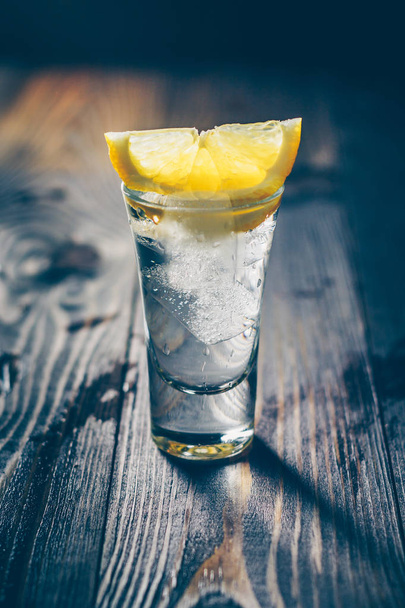 A wooden rustic table with an ice-cold glass of vodka and a slice of lemon - Photo, Image