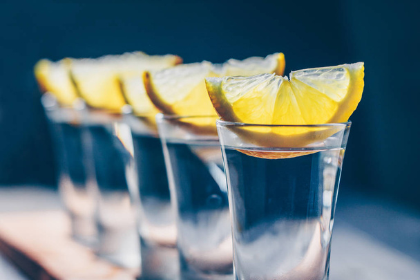 Close-up of selective focus on a row of glasses with tequila and lemon on the bar counter - Фото, зображення
