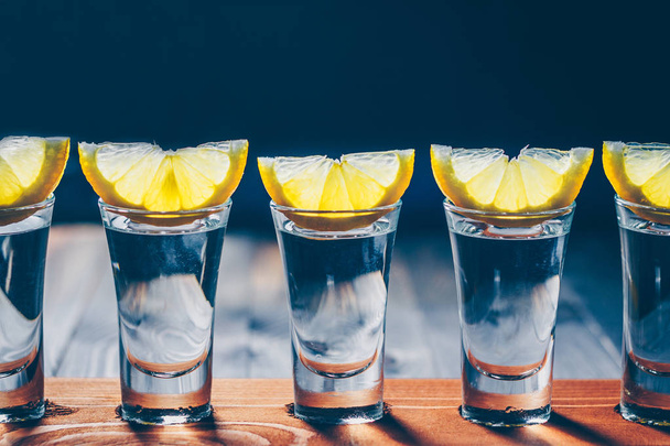 A row of wine glasses with vodka or tequila with lemon slices on a black background - Φωτογραφία, εικόνα