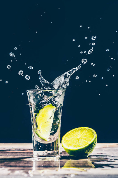 Lime slice falls into a glass with alcohol, gin, tequila, vodka - Zdjęcie, obraz