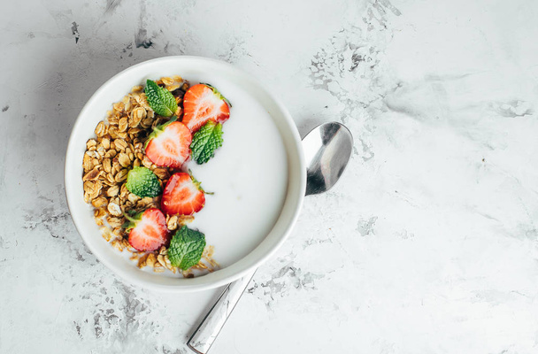 Здоровый завтрак концепции. Чаша с мюсли, йогуртом и ягодами на белом мраморном фоне. Вид сверху, плоский, копировальное пространство
 - Фото, изображение