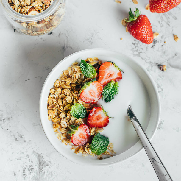 Концепція здорового сніданку. Миска з гранолою, йогуртом та ягодами на фоні білого мармуру. Вид зверху, плоский ліжко
 - Фото, зображення
