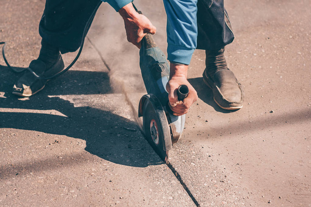 The worker cuts the asphalt with an angular grinder with a diamond disc - Fotó, kép
