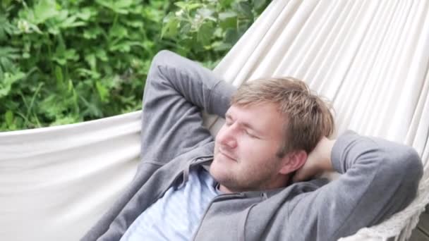 Χαλαρός άνθρωπος που βρίσκεται σε μια αιώρα το καλοκαίρι στη βεράντα - Πλάνα, βίντεο