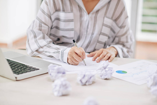 Gesichtslose Aufnahme einer Frau, die im Büro arbeitet und mit zerknüllten Papieren am Tisch Dokumente schreibt - Foto, Bild
