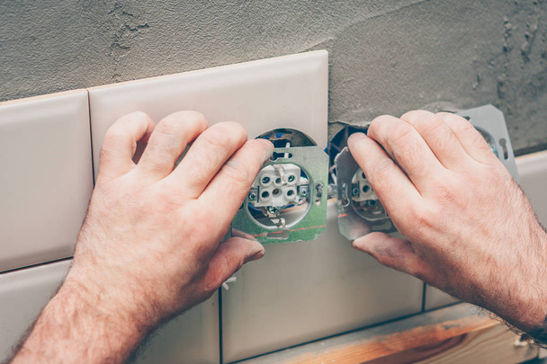 Finishing work - The electrician mounts an electrical outlet in a circular tile hole - Foto, Bild