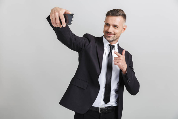 Εικόνα του επιτυχημένη Καυκάσιος επιχειρηματίας στο επίσημο κοστούμι που σημαδεύει το δάχτυλο και παίρνοντας selfie στο κινητό τηλέφωνο - Φωτογραφία, εικόνα